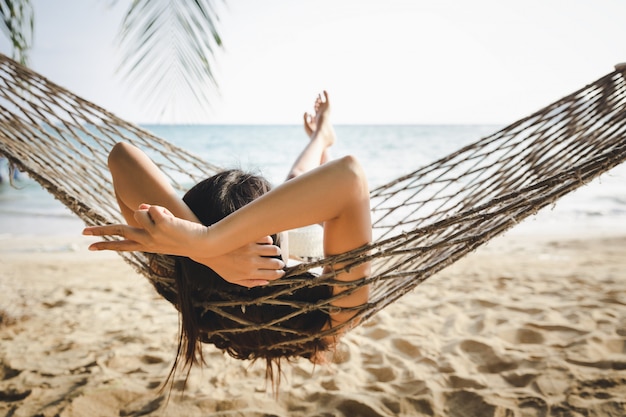 Summer travel vacation concept, Happy traveler asian woman with white bikini relax in hammock on beach in Koh mak, Thailand