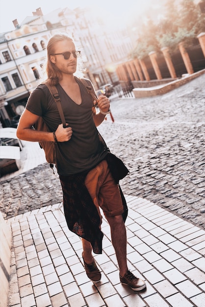 Summer trip. Full length of young man in casual clothing wandering empty street 