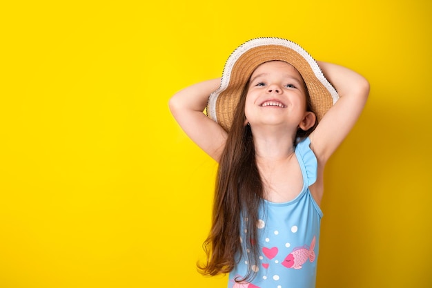 Summer vacation by the sea Portrait of a cheerful girl in a blue swimsuit and hat yellow background