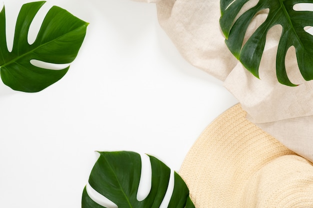 Summer vacation concept with tropical monstera leaves and straw hat on white background