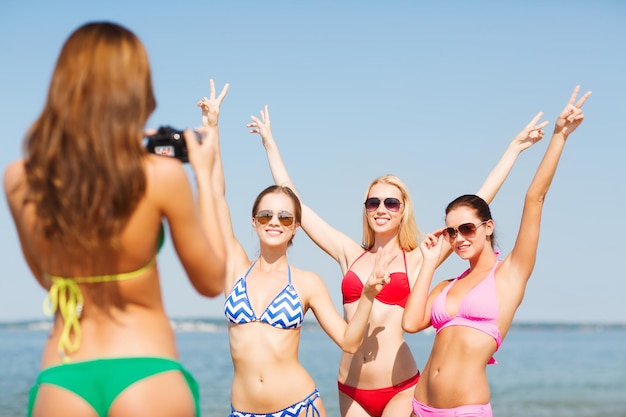 summer vacation, holidays, gesture and people concept - group of smiling women photographing by camera and showing peace sigh on beach