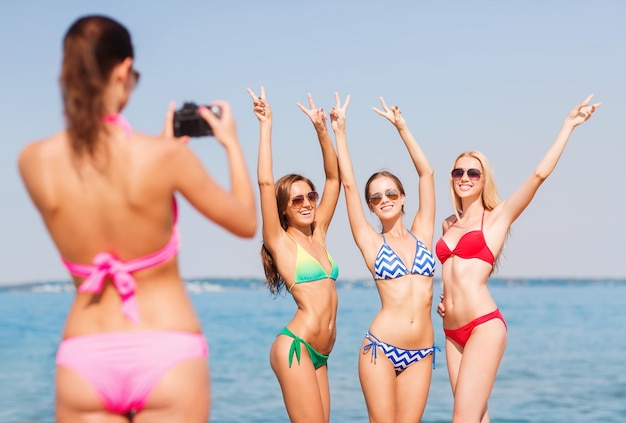 summer vacation, holidays, gesture and people concept - group of smiling women photographing by camera and showing peace sigh on beach