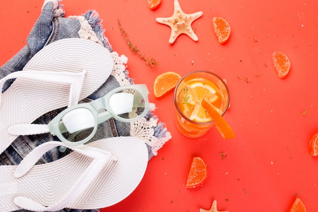 Summer vacation. Orange fruit cocktail, detox water near white flip flops, shorts and sunglases.