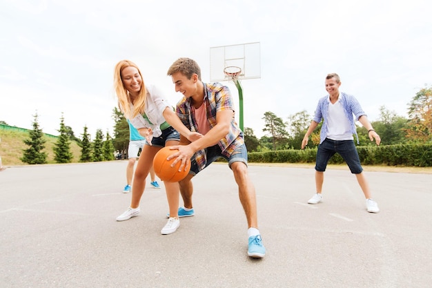 summer vacation, sport, games and friendship concept - group of happy teenagers playing basketball outdoors