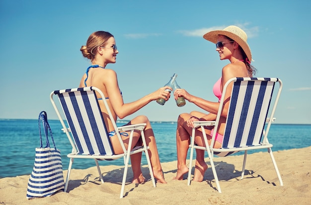 summer vacation, travel and people concept - happy women drinking beer and sunbathing in lounges on beach