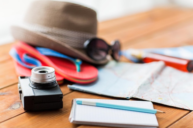 summer vacation, travel, tourism and objects concept - close up of camera, notepad with pencil and personal accessories