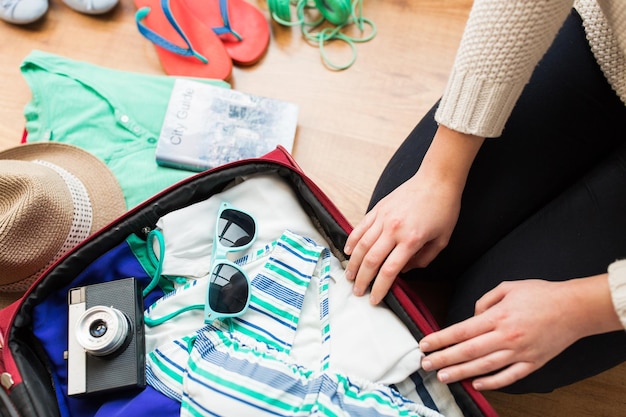 Photo summer vacation, travel, tourism and objects concept - close up of woman packing travel bag for vacation