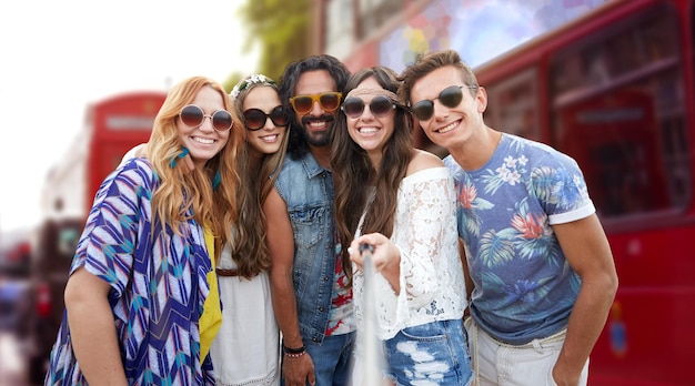 summer vacation, travel, tourism, technology and people concept - smiling young hippie friends taking picture by smartphone selfie stick over london city street background