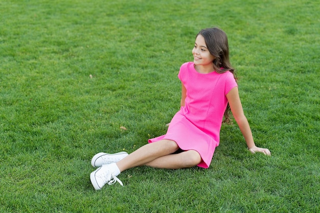 Summer vacation Vacation ideas Happy smiling girl enjoy relax on lawn Cheerful schoolgirl Have fun Girl cute kid sit green grass Emotional happy kid relaxing outdoors What makes child happy