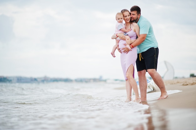 Summer vacations. Parents and people outdoor activity with children. Happy family holidays. Father, pregnant mother, baby daughter on sea sand beach.