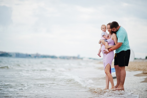 Summer vacations. Parents and people outdoor activity with children. Happy family holidays. Father, pregnant mother, baby daughter on sea sand beach.