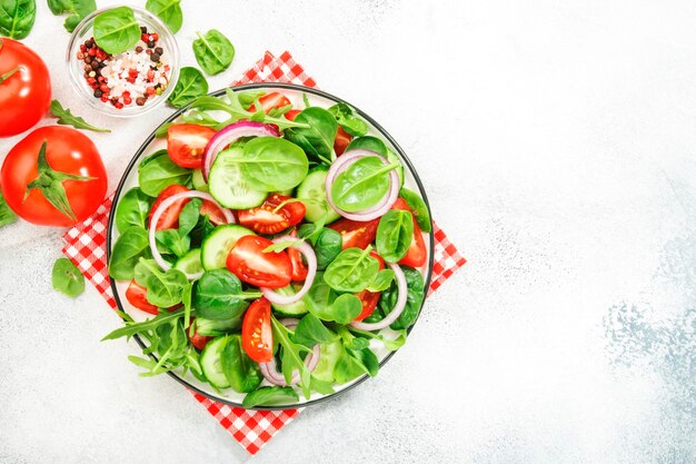 Summer vegan salad with spinach tomatoes arugula cucumber and red onion Fresh and Healthy food Gray stone table Top view