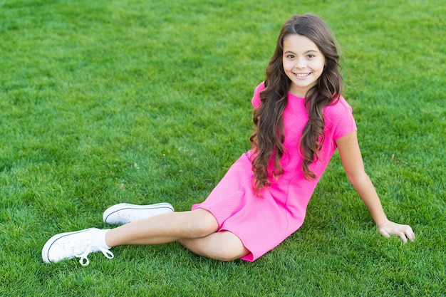 Summer vibes. Little girl relax on green grass. Parks and outdoor. Spring nature. Summer picnic. Schoolgirl smiling kid in pink dress. Happy childhood. Park with green grass. Relaxing on green grass.