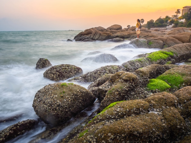 Summer view at the sea. Young woman enjoying sunset on a cliff.