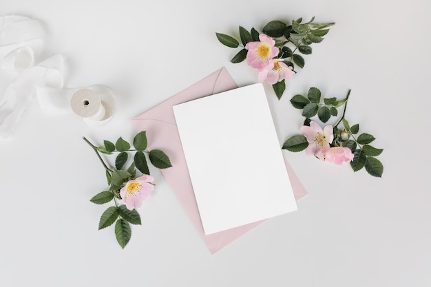 Summer wedding stationery mockup scene with silk ribbon Blank greeting card invitation pink envelope and blooming dog rose flowers isolated on white table background Flat lay top view