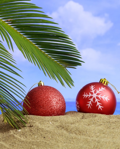 Summer xmas holidays concept Christmas ornaments on sandy beach with palm tree blue sea and sky background