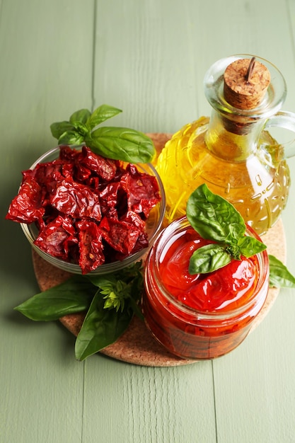 Sun dried tomatoes in glass jar olive oil in glass bottle basil leaves on color wooden background