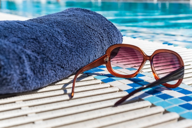 Sun glasses and towel near swimming pool.