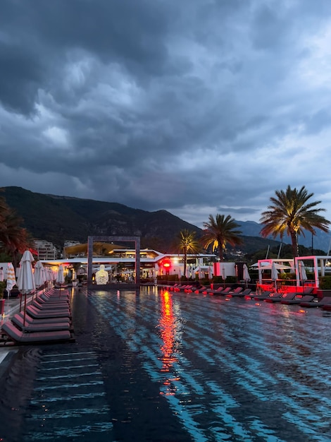 Sun loungers with folded umbrellas stand near the illuminated pool at dusk