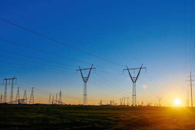 Sun rise on field with high voltage electricity towers Dark silhouettes of repeating power lines on sunrise Electricity generation transmission and distribution network Industrial landscape