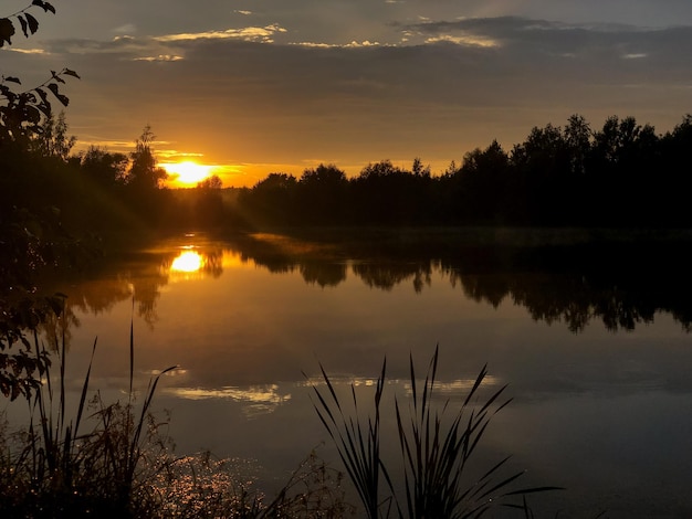 Sun sets over the horizon above calm lake on summer evening nature landscape