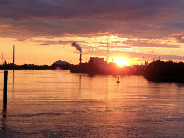 The sun sets over a river with a coal plant in the background