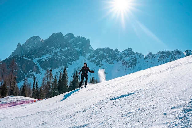 Sun shining over skier skiing on snow covered mountains during sunny day