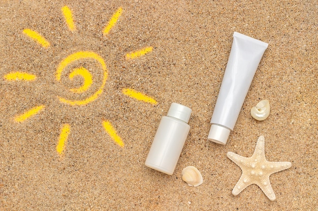 Photo sun sign drawn on sand, starfish and white tube, bottle of sunscreen.