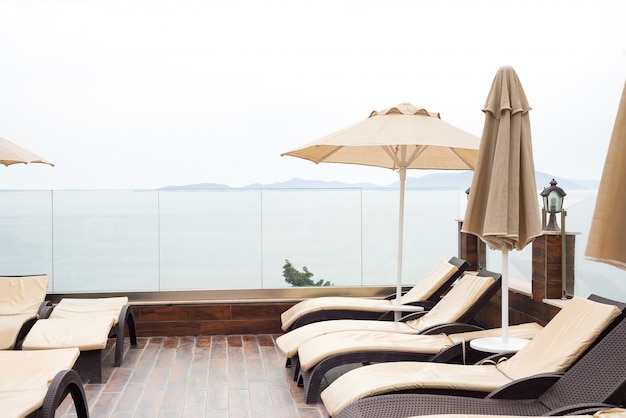 Sun umbrellas beige color and sunbeds near swimming pool with with sea views.