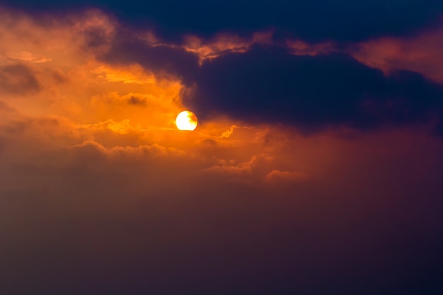 Sun with dark clouds in orange sky at evening with grain