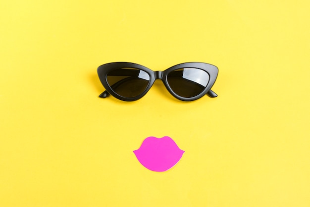 The sun with stylish black sunglasses,  pink lips on yellow Flat lay  