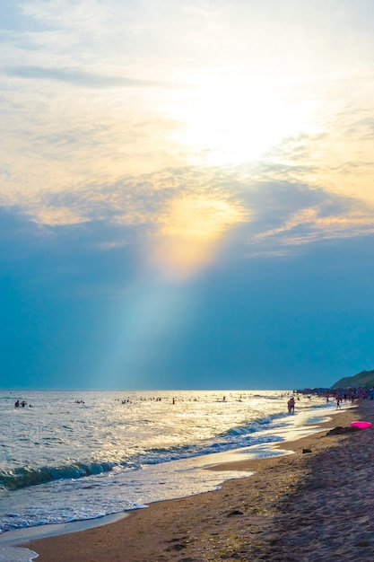 A sunbeam illuminates the sky with clouds in orange and a summer sea beach with tourists