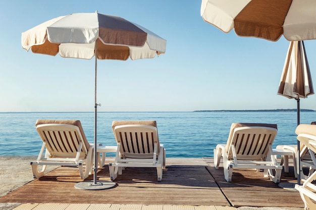 Sunbeds with umbrellas on the pier against the backdrop of the sea. Relax and pleasure.