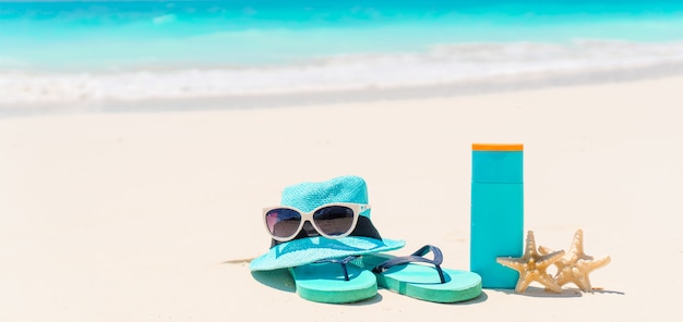 Suncream bottles, sunglasses, flip flop starfish on white sand background ocean