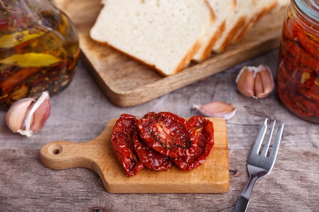 Sundried tomatoes in olive oil on a mini board with homemade bread in a rustic style Traditional home cooking Selective focus closeup