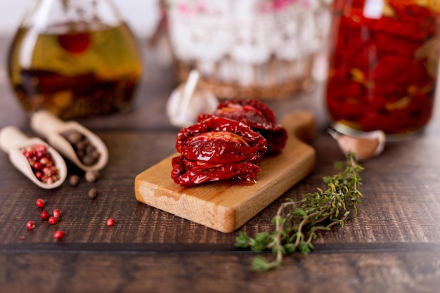 Sundried tomatoes in olive oil on a mini board with pepper garlic and thyme in a rustic style Selective focus closeup