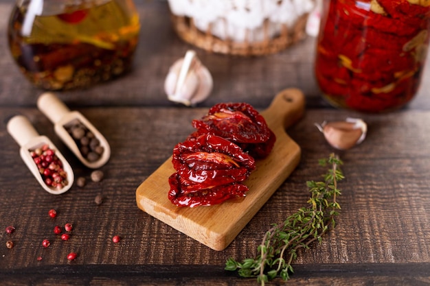 Sundried tomatoes in olive oil on a mini board with pepper garlic and thyme in a rustic style Selective focus closeup