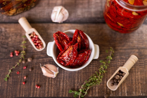 Sundried tomatoes in olive oil in a white bowl with pepper garlic and thyme in a rustic style Selective focus closeup