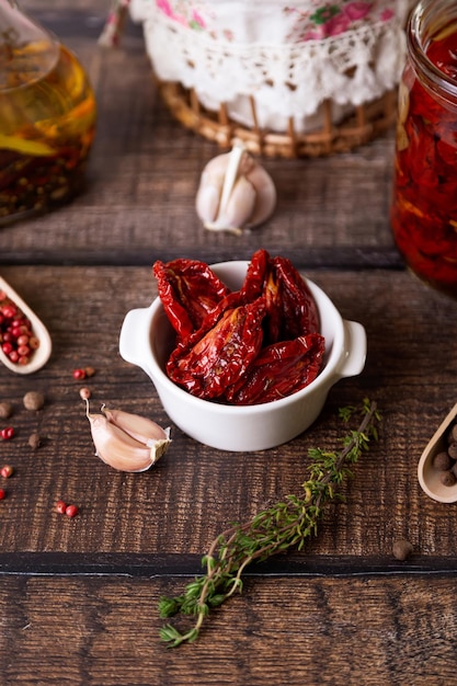 Sundried tomatoes in olive oil in a white bowl with pepper garlic and thyme in a rustic style Selective focus closeup