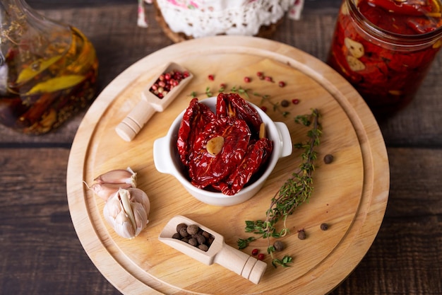 Sundried tomatoes in olive oil in a white bowl with pepper garlic and thyme on a wooden board Home cooking rustic style Selective focus closeup