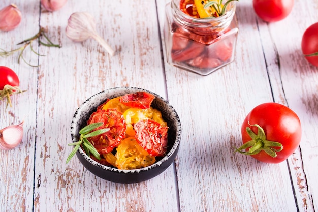 Sundried tomatoes with spices and herbs in a bowl and fresh vegetables on the table Homemade snack