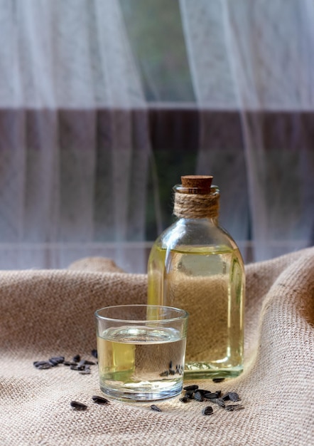 Sunflower oil in a bottle glass with seeds on burlap canvas fabric background