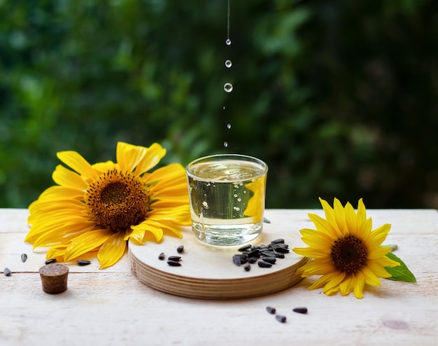 Sunflower oil drops pouring into a glass with sunflowers and seeds on background