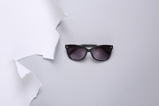 Sunglasses and torn paper sheet on gray background Fashion concept Copy space