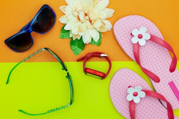 Sunglasses with beach shoes and flower on colorful paper background