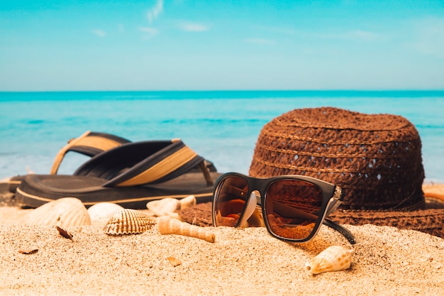 Sunglasses with hat and flip flops on sandy beach