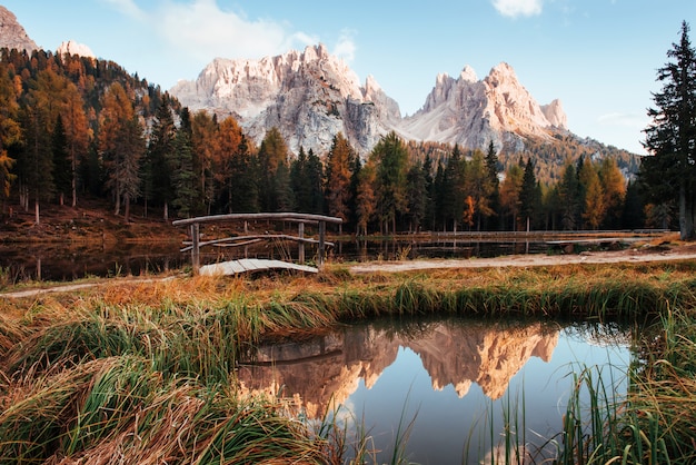 Sunlight on the top. Amazing view of majestic mountains with woods in front of them at autumn day. Puddle that goes from the lake with little bridge in the center