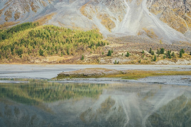 Sunny autumn landscape with mountain lake with view to sunlit gold forest hillside. Golden autumn scenery with clear water of lake. Blue calm transparent water in sunshine on background of mountain.