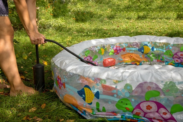 On a sunny day a woman inflates a children's pool standing on the grass with a pump