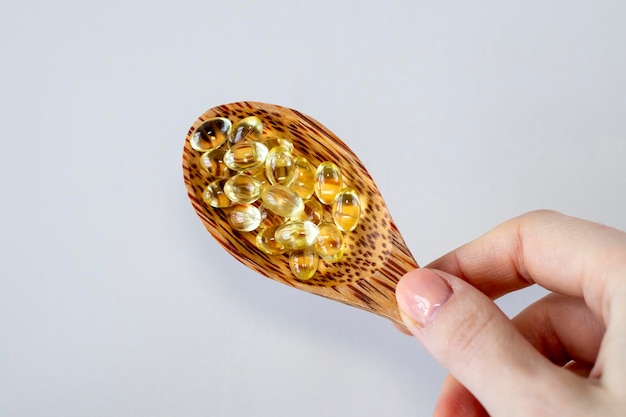 Sunny vitamin D3 supplement capsules in a wooden spoon in a woman's hand on a white background